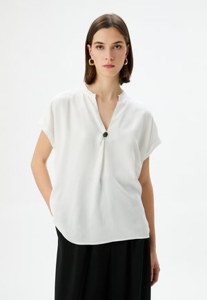 Blusa bianca a maniche corte con scollo a V e dettaglio di bottoni neri al collo, realizzata in un tessuto liscio e leggero. Design morbido e fluido.
