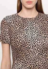 Majica kratkih rukava s smešnim pozadinom i crnim leopard uzorcima. Glatka tekstura s okruglim izrezom. Bez ukrasa ili dodataka.
