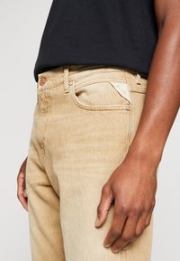Denimjeans i en ljus beige färg med rak bendesign, som har en klassisk femficksstil och knäppning samt subtil slitning.