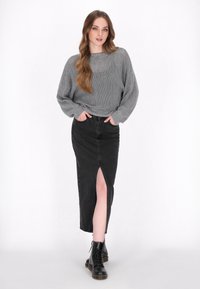 Maglione grigio a maglia con vestibilità ampia, abbinato a una gonna di jeans nera con spacco frontale. La modella indossa stivaletti neri con lacci.