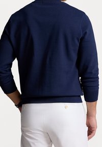 Mörkblå sweatshirt med ribbade muddar och fåll, med en enkel rund halsringning. Matchad med vita byxor som visar en ren stil.