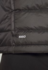 Gros plan d'une section d'une veste matelassée noire avec le numéro 550 cousu en fil blanc sur le tissu.