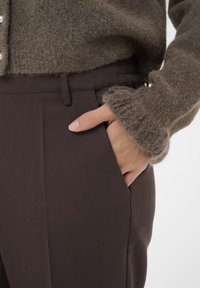 Brown elastic-waist trousers with side pockets, paired with a fuzzy, light brown sweater featuring a ribbed cuff and button detail.
