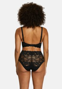 Set di lingerie in pizzo nero composto da un reggiseno con spalline regolabili e un perizoma a vita alta con motivi floreali e bordi ondulati.