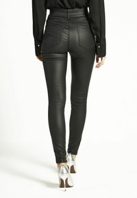 Pantaloni neri in similpelle a vita alta, con vestibilità slim, tasche posteriori e superficie lucida, abbinati a scarpe con tacco alto argentate.