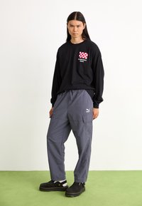 Schwarzes Langarmshirt mit roten und weißen Karomuster-Taschenkanten, kombiniert mit grauen Cargo-Hosen und schwarzen Clogs; flache Textur.