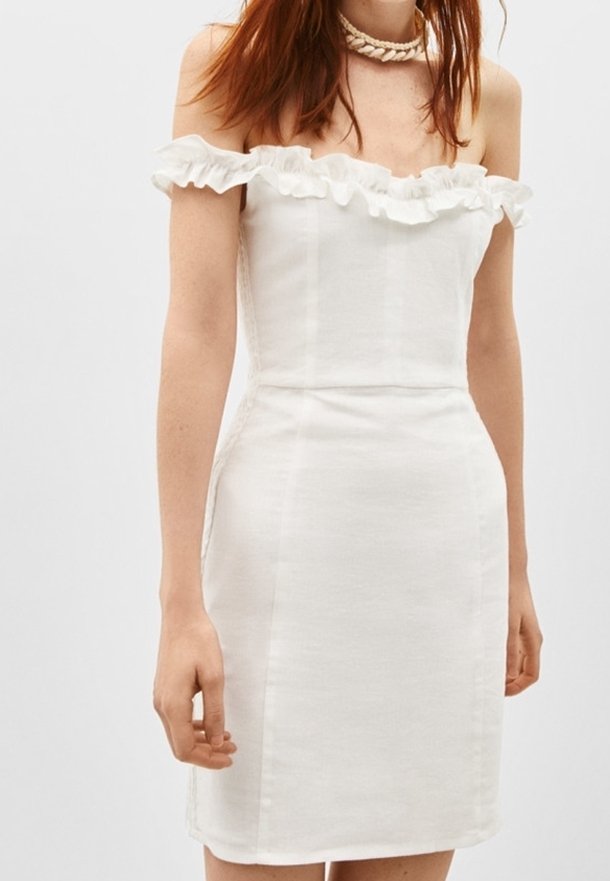Femme portant une robe blanche épaules dénudées avec un col à volants et un collier tressé, montrée des épaules jusqu'à mi-cuisse.