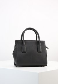 Borsa a tracolla in pelle nera con due manici arrotondati e chiusura con zip, posizionata su un piedistallo bianco contro uno sfondo semplice.