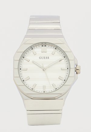 Sølv Guess-armbåndsur med rund hvid urskive, sølv timeindeks og tre visere, der viser kl. 10:10:35.