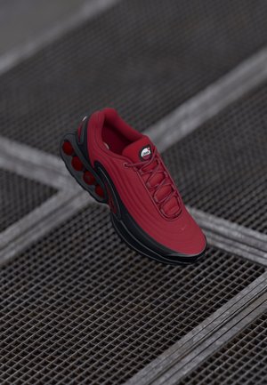 Red sneaker with a textured upper, featuring black accents and a prominent air cushioning sole design. Laces and logo are visible on top.