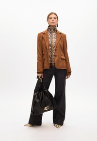 Hnědý semišový blazer, top s hadím vzorem, tmavé džíny, zlaté lodičky se špičatou špičkou a černá kožená taška s detailem zlatého loga.