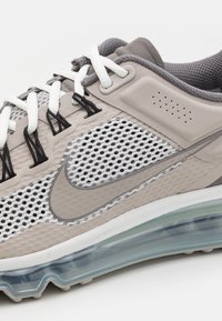 Baskets Nike gris et blanc avec design en mesh, lacets blancs, semelle à coussin d'air visible et logo Nike swoosh gris sur le côté.