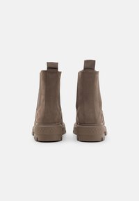 Bottes chelsea en daim marron avec des panneaux latéraux élastiques, des tirants et des semelles en caoutchouc texturé. Design simple et épuré avec des détails de couture minimalistes.