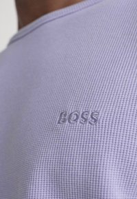 Levendula színű, textúrázott ing, bordázott mintázattal és a bal alsó oldalon emboszált "BOSS" logóval. Kerek nyakú, rövid ujjú.