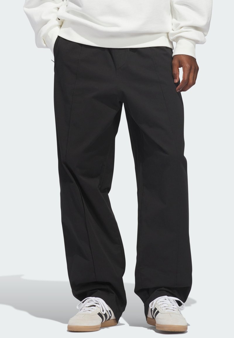 Μαύρο παντελόνι με φαρδύ πόδι από ελαφρύ ύφασμα, με πιέτες στο μπροστινό μέρος και πλαϊνές τσέπες, συνδυασμένο με λευκά αθλητικά π απούτσια με μαύρες ρίγες.