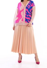 Stickad kortkappa med rosa och blå djurtryck, med V-ringning och fem knappar. Kombineras med en plisserad beige midijurk och rosa klackar.