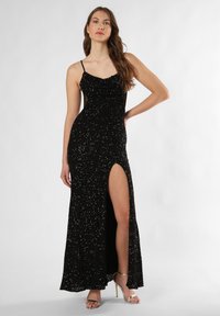 Schwarzes, glitzerndes Abendkleid mit Schalkragen, dünnen Trägern und einem hohen Schlitz bis zum Oberschenkel. Enganliegendes Design, bodenlang, strukturierte Oberfläche.