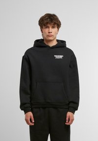 Black cotton hoodie with a front pocket, featuring white text on the chest. Simple design with a relaxed fit and adjustable hood.