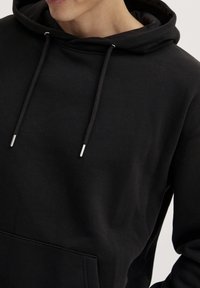 Sudadera negra hecha de material suave, con un bolsillo delantero, cordones ajustables y puntas metálicas plateadas, que presenta un corte relajado.