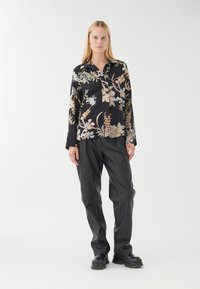 Schwarzblumiges Hemd mit langen Ärmeln, verziert mit hellen Blumen und Blättern; kombiniert mit lockeren schwarzen Hosen und schwarzen Schuhen.
