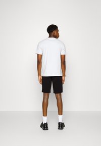Lys grå kortermet t-skjorte, svarte shorts, svarte sko, hvite sokker, sett fra ryggen i en minimalistisk setting.