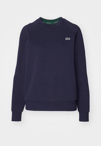 Mørkeblå sweatshirt laget av bomull, med rund hals, ribbestrikkede ermer og en liten grønn Lacoste-logo på brystet.