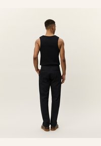 Zwarte mouwloze tanktop en donkere broek gezien vanuit de achterkant. De stof is glad met een aansluitend ontwerp, de broek heeft twee achterzakken.
