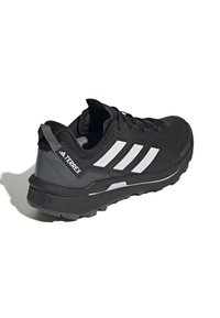 Czarne buty sportowe z teksturowaną cholewką, wyposażone w trzy białe paski, wzmocnioną piętę i solidną podeszwę zapewniającą przyczepność.