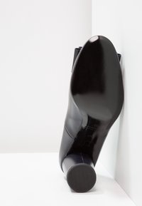 Scarpa con tacco alto in pelle nera con finitura lucida, punta arrotondata e tacco cilindrico. La suola presenta un motivo di grip testurizzato.
