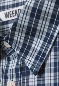 Blauw en lichtblauw geruite korte mouw shirt met een puntige kraag en plastic knopen, voorzien van een label met de tekst "WEEKDAY."