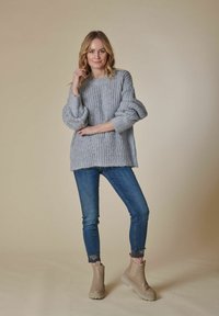 Hellgrauer, grob gestrickter Pullover, lockere Passform, gerippte Bündchen, kombiniert mit blauen Jeans und beigen Ankle-Boots mit dicker Sohle. Einheitlicher Hintergrund.