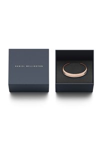 Zlati in srebrni zapestnica v notranjosti mornarsko modre škatlice z črnim notranjostjo. Na vrhu škatlice je v zlati barvi vtisnjeno ime "DANIEL WELLINGTON".