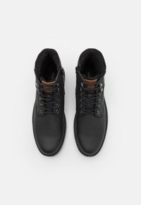Botas de cuero negro con un interior suave forrado de piel, presentando un acento de cuero marrón, ojales de metal y una suela resistente.