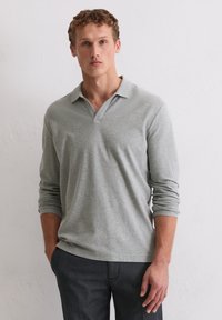 Grau langärmliges Polohemd mit V-Ausschnitt. Weicher Stoff, minimale Nähte und schmal geschnittene Ärmel, kombiniert mit dunklen Hosen.