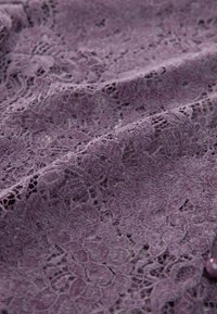 Lila Spitzenstoff weist komplexe florale Muster mit einer weichen, strukturierten Oberfläche auf. Zarte Durchbrüche verbessern die visuelle Komplexität.