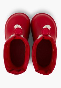 Zapatos de goma rojos con forma redondeada, exterior texturizado y forro de felpa suave. Presentan un pompón decorativo y un acento circular.