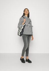 Bluză cu dungi alb-negru și detalii cu fundiță, blugi skinny gri, loafers negri strălucitori și o geantă tote cu dungi alb-negru.