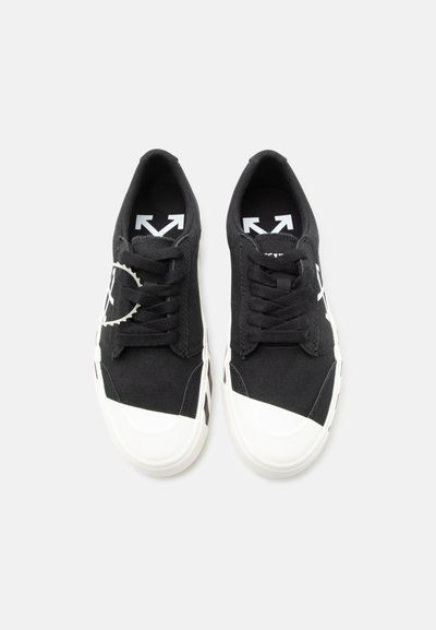 Ζευγάρι μαύρα πάνινα αθλητικά παπούτσια με λευκά λαστιχένια μυτερά άκρα και σόλες, μαύρα κορδόνια και λευκά λογότυπα βέλους στις πελματικές εσωτερικές επιφάνειες και στις πλευρές.