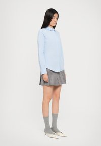 Svijetloplava košulja na dugih rukava, mini suknja s houndstooth uzorkom, sivi čarape do članaka i bež balerinke s oštrom olupinom. Glatka tkanina, ležeran kroj.