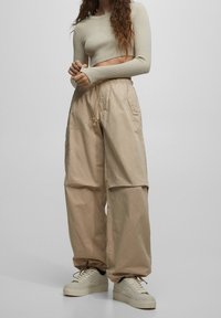 Beige cargobroek met een ontspannen pasvorm, verstelbare tailleband en elastische manchetten; gecombineerd met een licht geribbelde cropped top en neutrale sneakers.