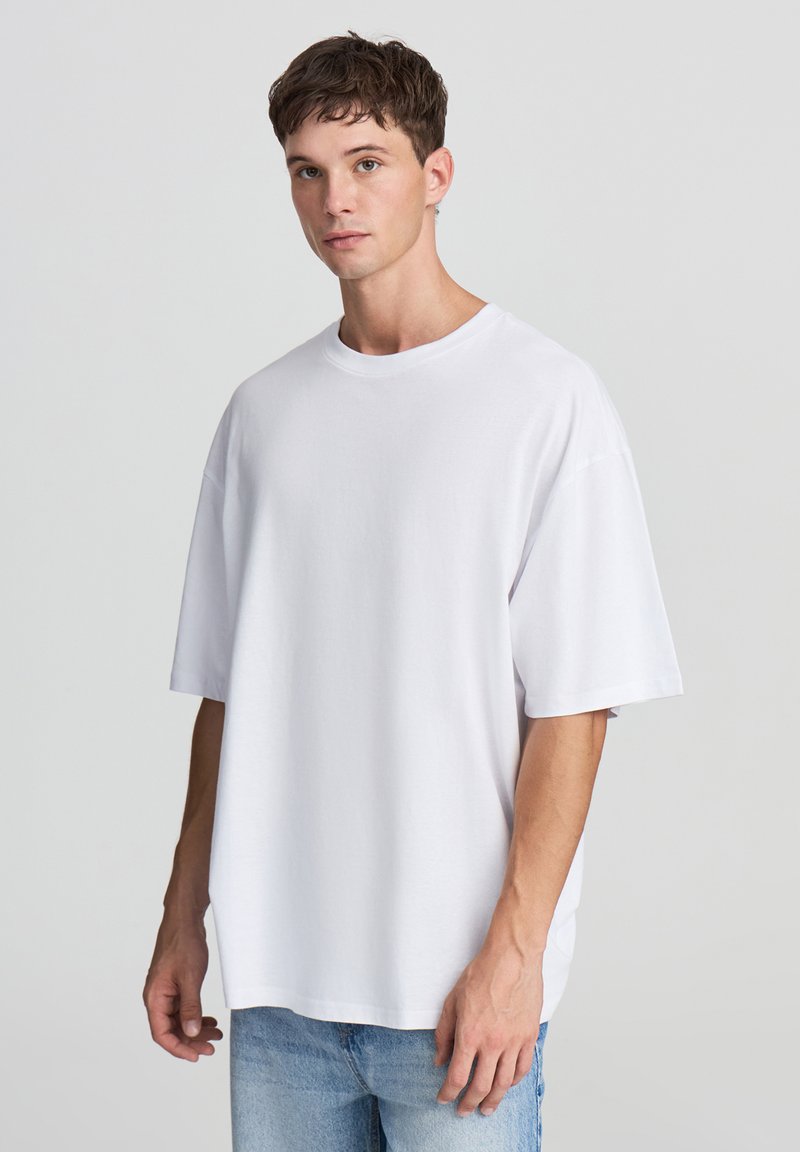 T-shirt bianco oversize in cotone con scollatura a girocollo e maniche corte, abbinato a jeans in denim azzurro chiaro. Design semplice e privo di ornamenti.