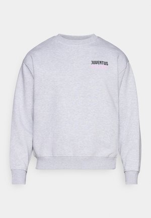 Sweatshirt gris avec un col ras du cou, des poignets et un ourlet côtelés. Présente le texte "JUVENTUS" en noir et rose sur la partie gauche de la poitrine. Texture douce.