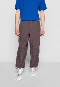 Pantalons gris foncé, amples, avec une taille élastique et un cordon de serrage. Associés à un t-shirt bleu à manches courtes et des baskets blanches.