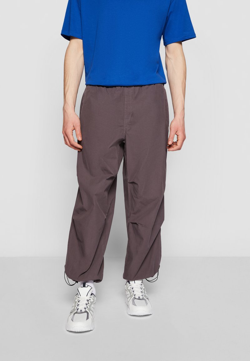 Pantalons gris foncé, amples, avec une taille élastique et un cordon de serrage. Associés à un t-shirt bleu à manches courtes et des baskets blanches.