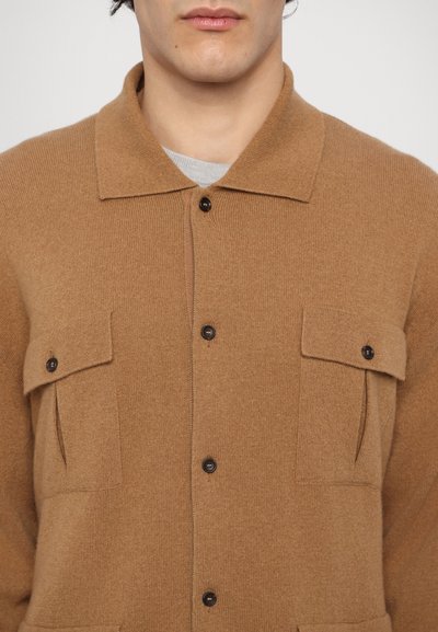 Camisa chaqueta de mezcla de lana marrón con cuello, dos bolsillos en el pecho y cierres de botón marrón, que presenta una textura suave y un diseño simple.