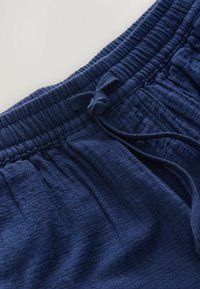 Shorts bleu marine texturés avec une taille élastique et un cordon de serrage à nouer. Présente un motif en grille et est en tissu de coton doux.
