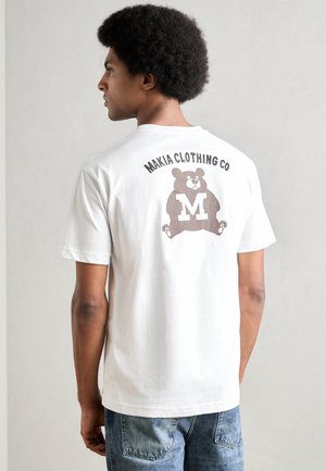White cotton T-shirt featuring a brown bear graphic and "MAKIA CLOTHING CO" text on the back. Short sleeves and round neckline.