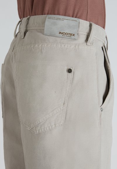 Pantalones de algodón color beige claro, que cuentan con un diseño clásico de cinco bolsillos y un pequeño detalle de logo en el bolsillo trasero.