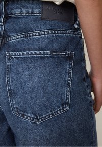 Dark blue denim jeans featuring a stitched back pocket, leather brand patch embossed with "Marc O'Polo DENIM," and faded texture.