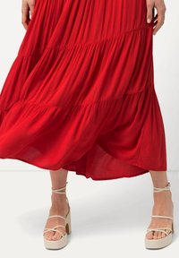 Abito maxi a strati rossi con texture plissettata. Abbinato a sandali platform beige con cinturini incrociati alla caviglia.